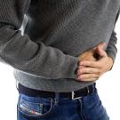 A man wearing a gray sweater and jeans is holding his stomach in pain. 