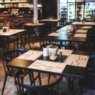 Restaurant interior with dark tables and chairs. There are menus at each of the place settings.