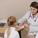 Woman in White Lab Coat Listening to a Girl and Writing Down Notes