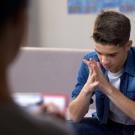 An adolescent boy sits on a couch looking depressed. 