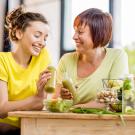 Woman and her daughter drinking some green juice next to a basket of vegetables