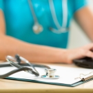 doctor at desk typing notes with clipboard in view