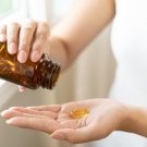 Person shaking vitamin D pills into their hand from a pill bottle
