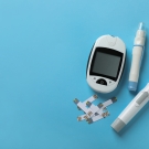 Insulin, blood glucose test trips, an insulin injection pen, and a blood glucose monitor against a blue background