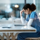medical professional sitting at a computer and holding her head