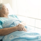 Older asian woman lying in a hospital bed looking out a window