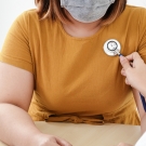 Overweight woman with a mask and a stethoscope being held to her heart by a doctor's hand