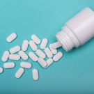 white pills spilling out of a pill bottle against a blue background