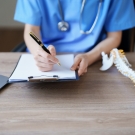 doctor writing with spine model on desk