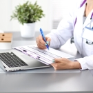 doctor writing on chart while sitting at a computer