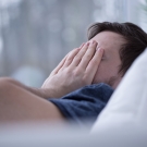 man covering face on bed
