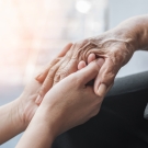 older patient and younger individual holding hands