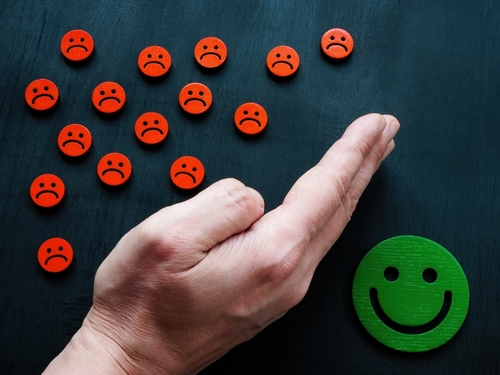 Hand blocking small red frowming icons from reaching large green smiling icon