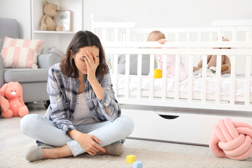 Stressed mom sitting next to crib with baby