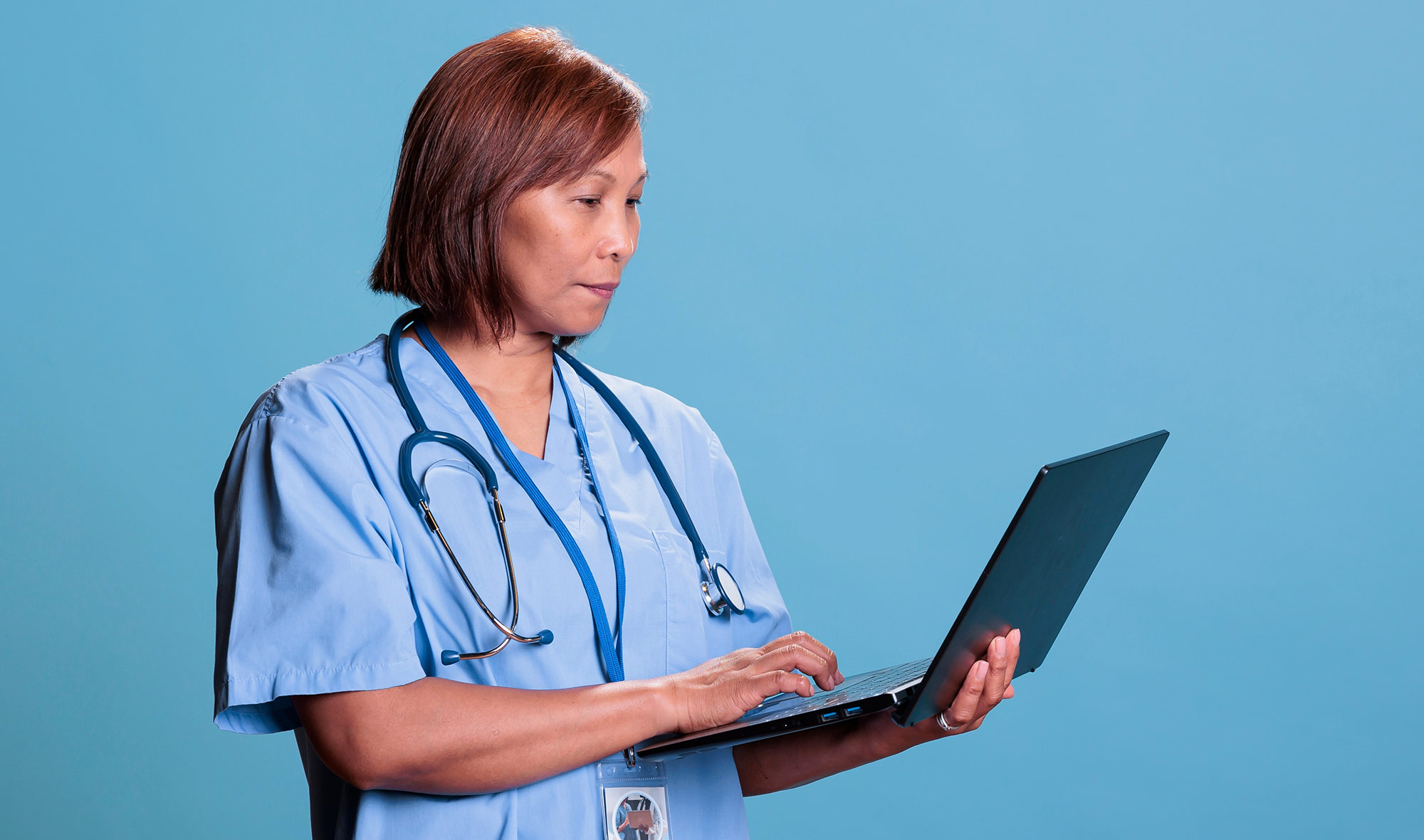 Healthcare professional in scrubs using a laptop