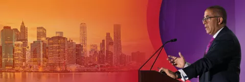 Faculty member speaking at podium alongside the NYC skyline