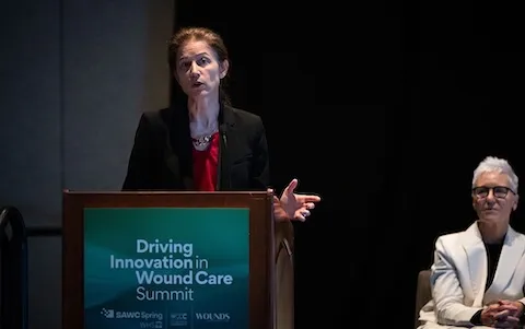 Woman speaks at a podium with the WCCC Driving Innovation in Wound Care Summit logo on it