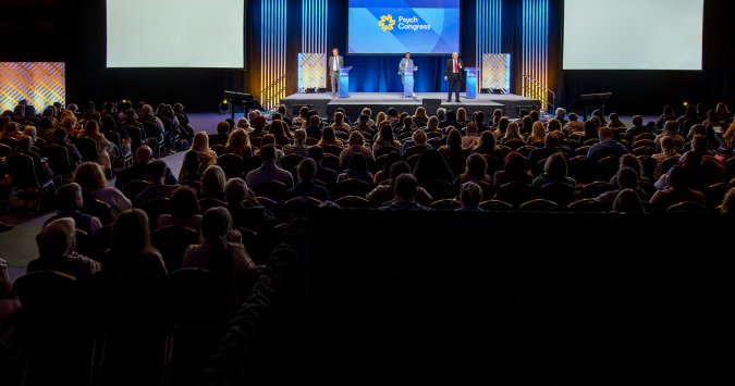 Full conference room watching three speakers on the main stage at Psych Congress