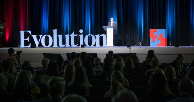 Man standing on stage at a conference with "Evolution" in big letters beside him