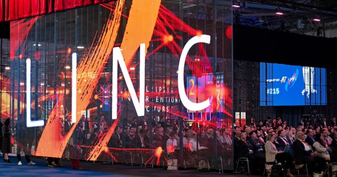 Full conference room of people watching a live case demonstration on the big screen