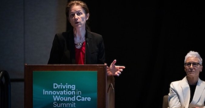 Woman speaks at a podium with the WCCC Driving Innovation in Wound Care Summit logo on it