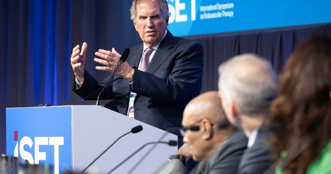 Dr. Barry Katzen speaking before a panel of people seated on a stage